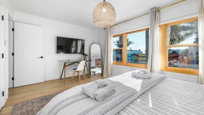 A modern bedroom with a bed, a desk, a chair, a television, and a large window with a view of the outside.