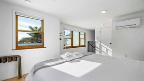 A bedroom with a bed, a window, a radiator, and an air conditioning unit.