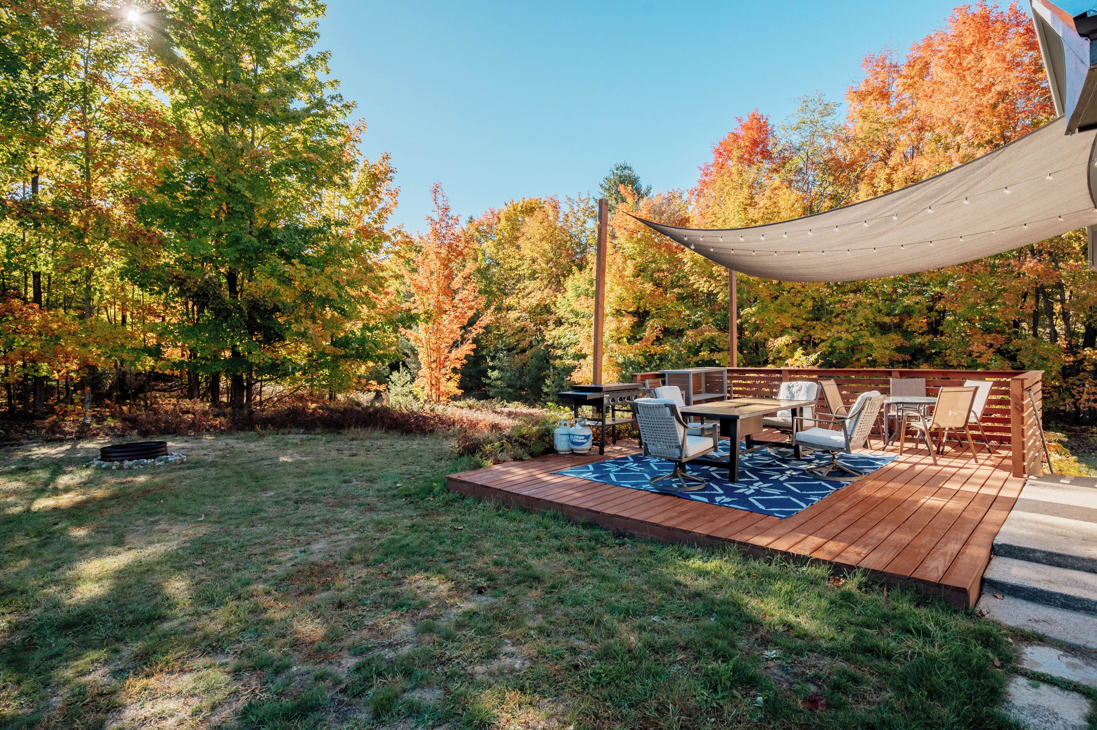 A wooden deck with outdoor furniture, surrounded by trees with autumn foliage.