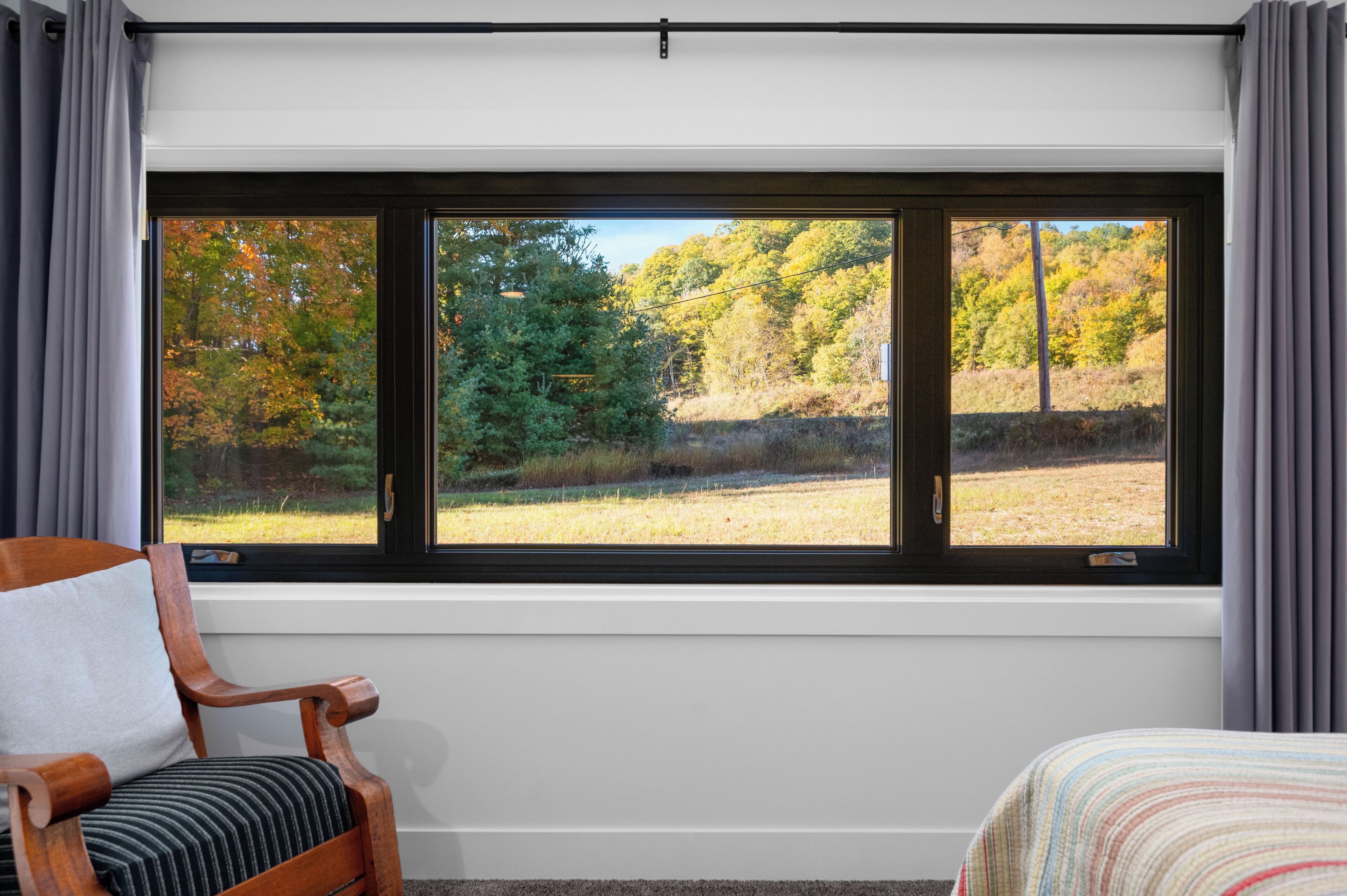 A room with a large window, a wooden chair, and a bed.