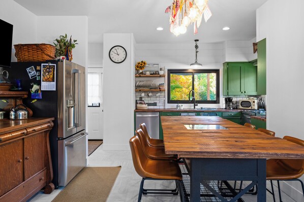 A modern kitchen with a wooden dining table, green cabinets, and a clock on the wall.