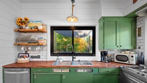 Une cuisine avec une fenêtre, des meubles de couleur verte, un four à micro-ondes et une cuisinière.