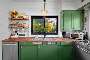 A kitchen with a window, green cabinets, a microwave, and a stove.