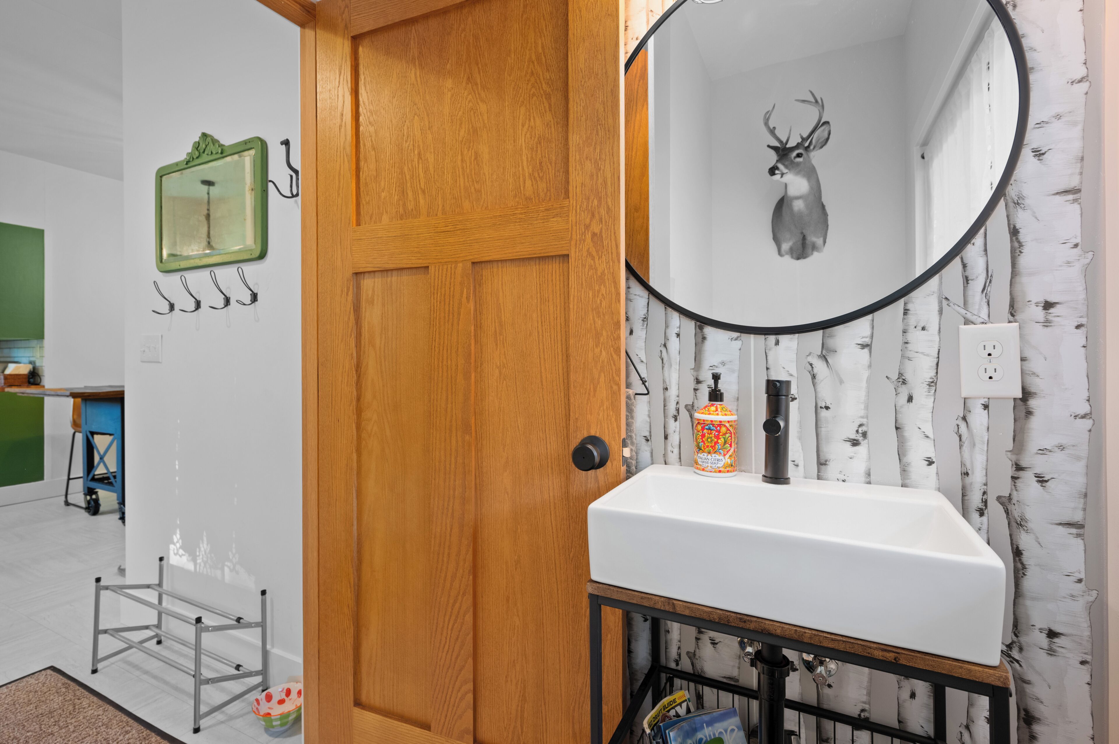 Une salle de bain avec une porte en bois, un lavabo blanc, un miroir et un miroir mural orné d’une tête de cerf.