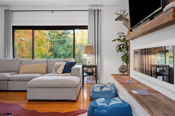 A modern living room with a sectional sofa, a wooden bench, a television, and a deer head decoration.