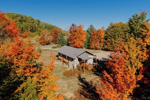 A modern house with a large deck, surrounded by autumn foliage.