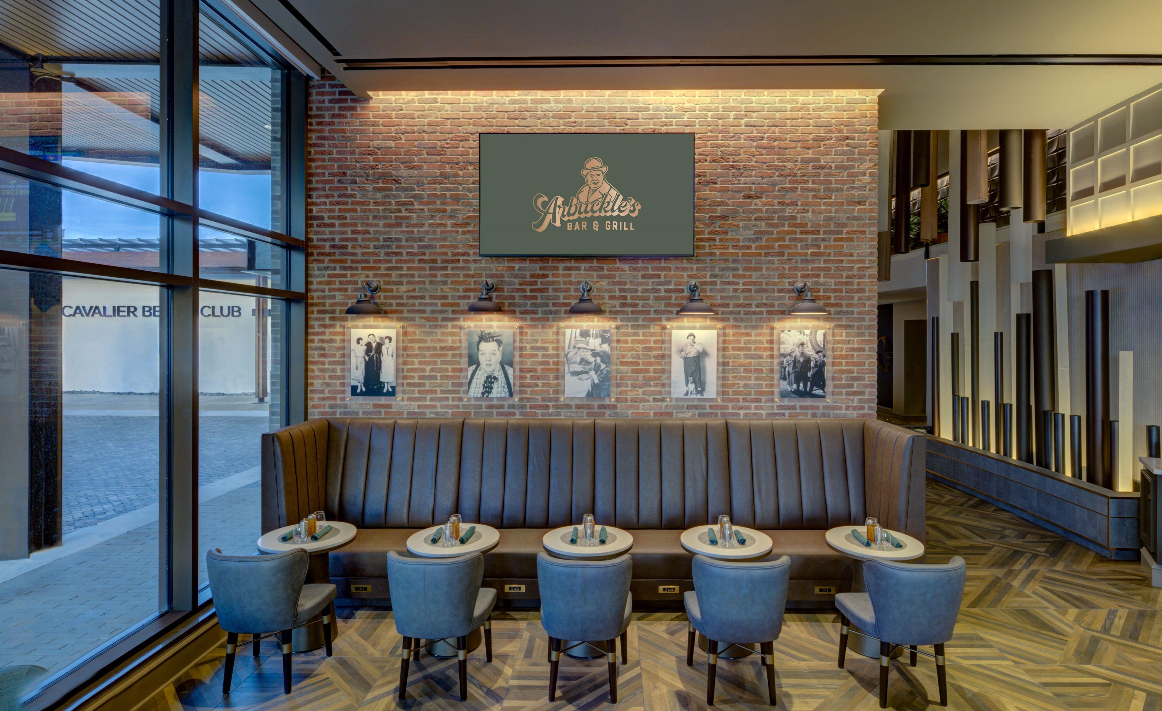A restaurant with a brick wall, a bar sign, and a row of tables and chairs.