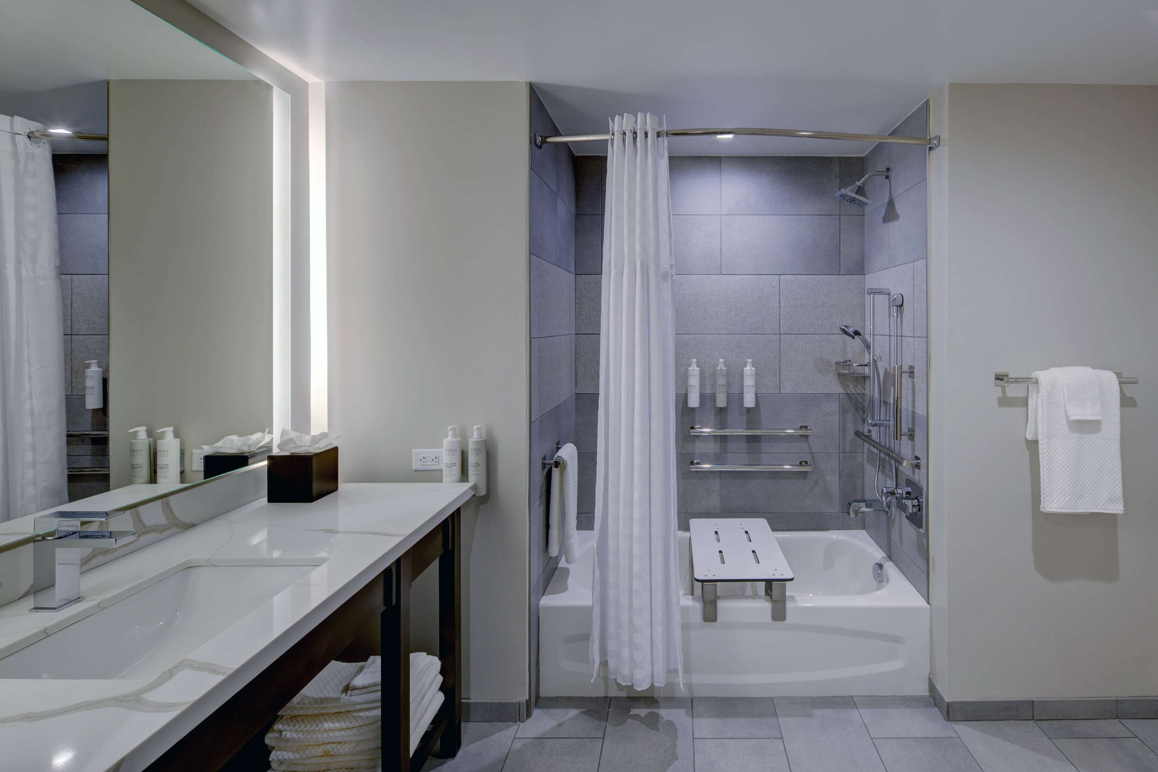 A modern bathroom with a large mirror, two sinks, a shower, and a bathtub.