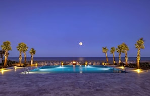 Zona junto a la piscina con una luna en el cielo, palmeras y vistas al mar.