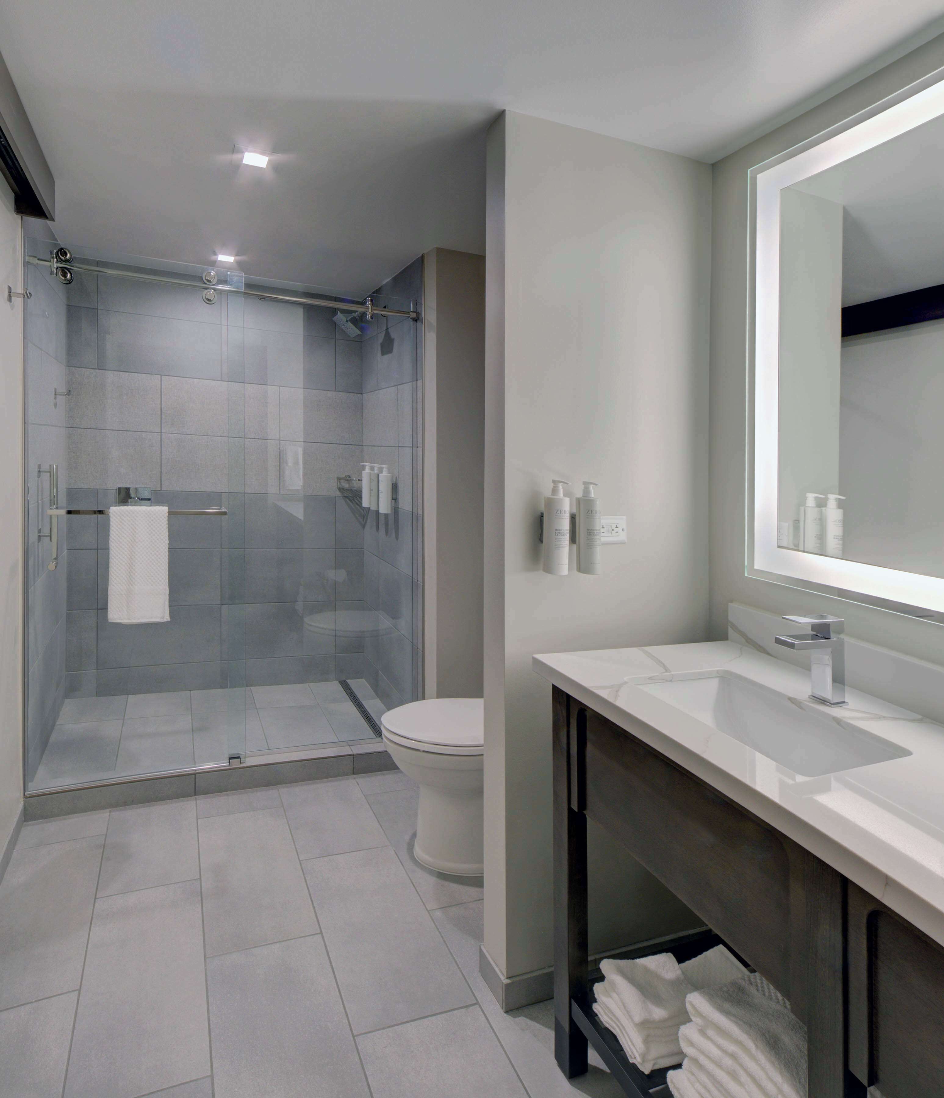 Un baño moderno con cabina de ducha de vidrio, inodoro y tocador con un espejo grande.