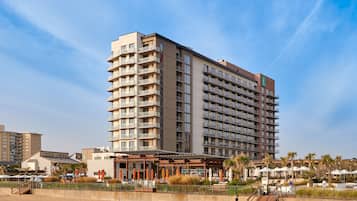 Un hotel de gran altura con múltiples balcones, ubicación frente a la playa y zona de piscina.
