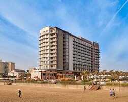 Un hotel de gran altura con múltiples balcones, ubicación frente a la playa y zona de piscina.