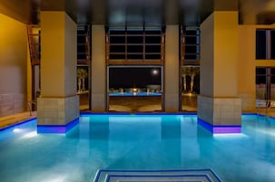Piscina interna com vista para a praia à noite.