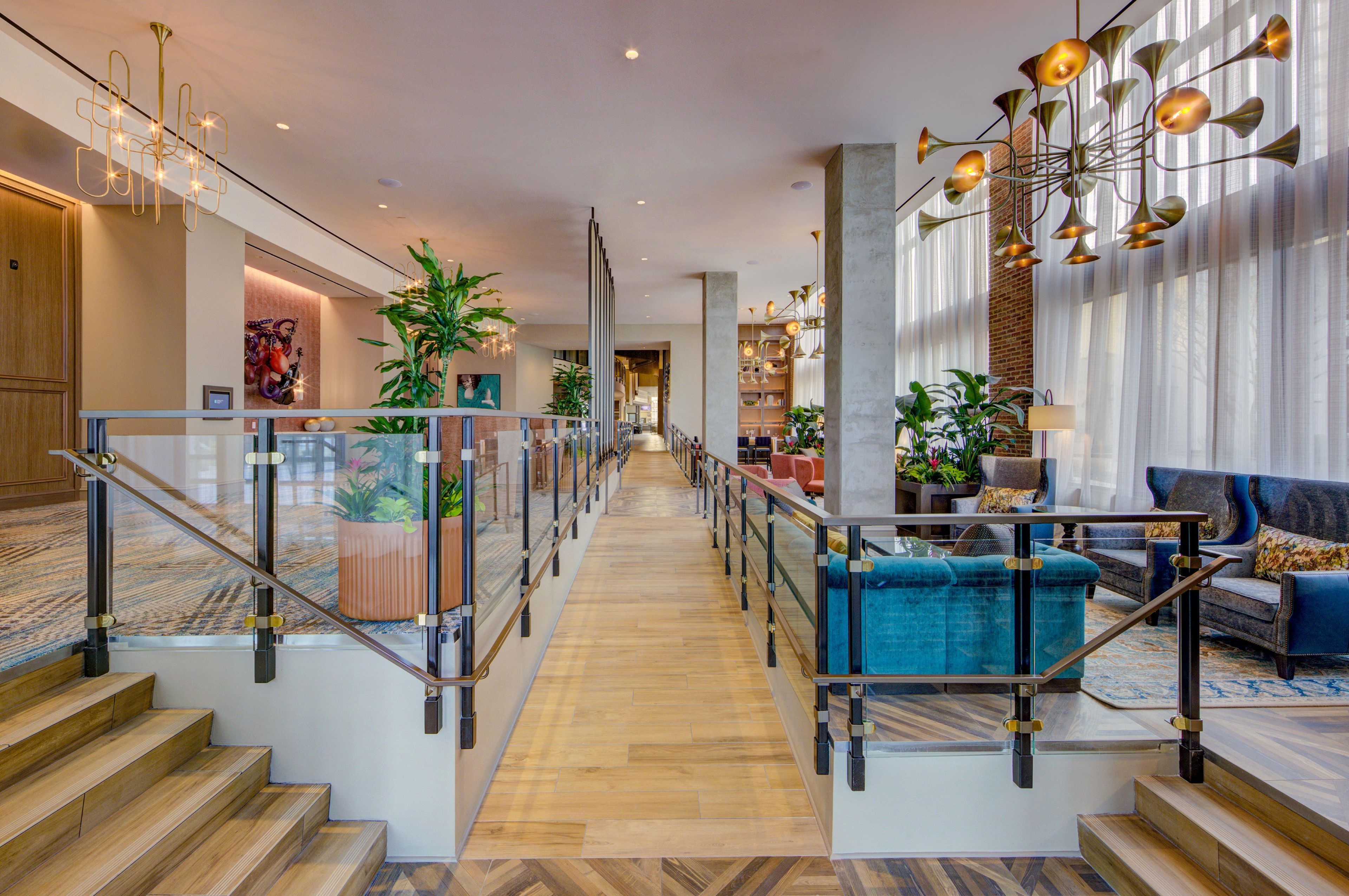 A spacious hotel lobby with a grand staircase, modern lighting fixtures, and comfortable seating areas.