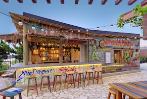 An outdoor bar with graffiti, a thatched roof, and string lights. - Embassy Suites by Hilton Virginia Beach Oceanfront Resort (Virginia Beach)