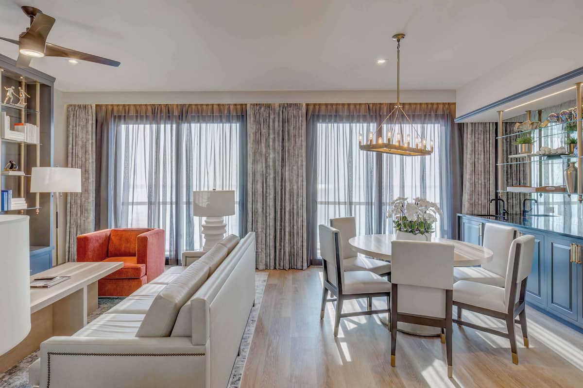 A modern living room with a sofa, a dining table, and chairs. There is a kitchen area with cabinets and a countertop.