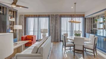 A modern living room with a sofa, a dining table, and chairs. There is a kitchen area with cabinets and a countertop.