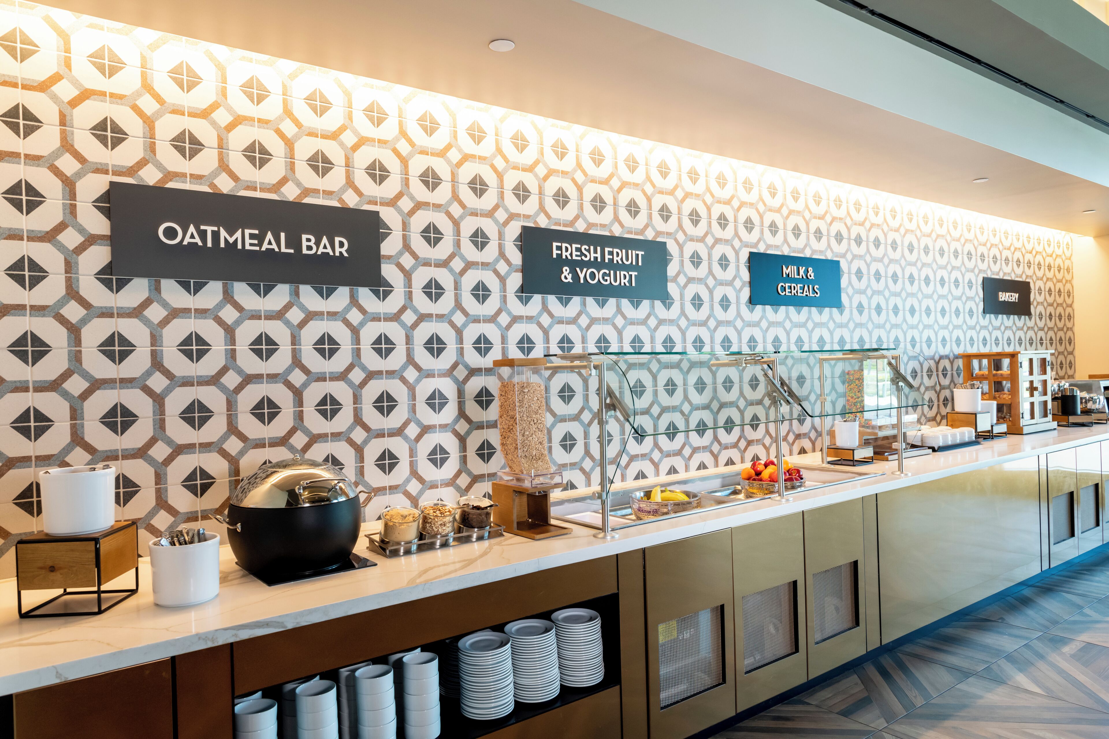 Ein Frühstücksbuffet mit Schildern für 'Oatmeal Bar', 'Frisches Obst & Joghurt' und 'Milch & Cerealien'.