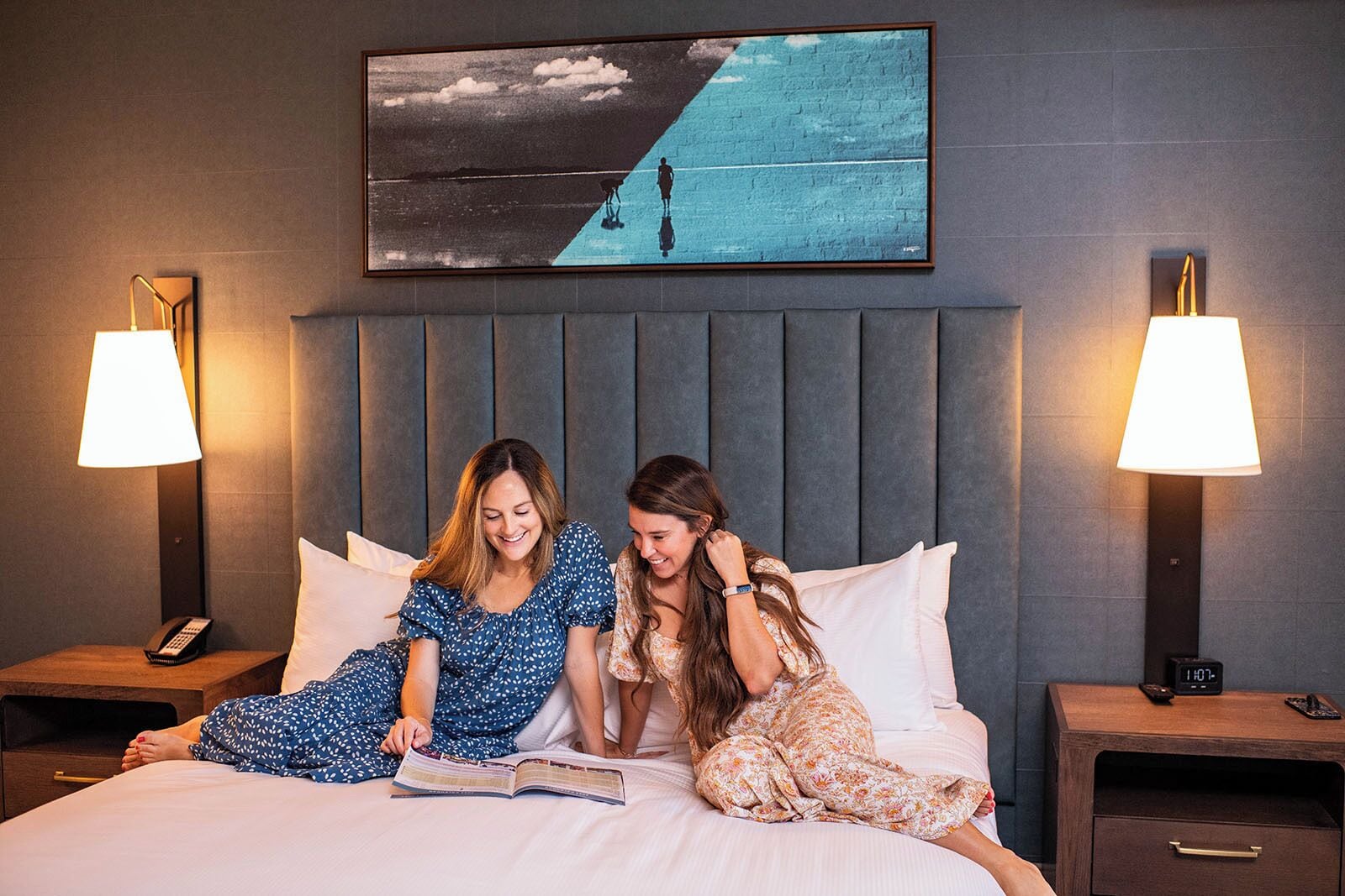 A hotel room with a large bed, two bedside lamps, a nightstand with a phone, and a painting above the bed.