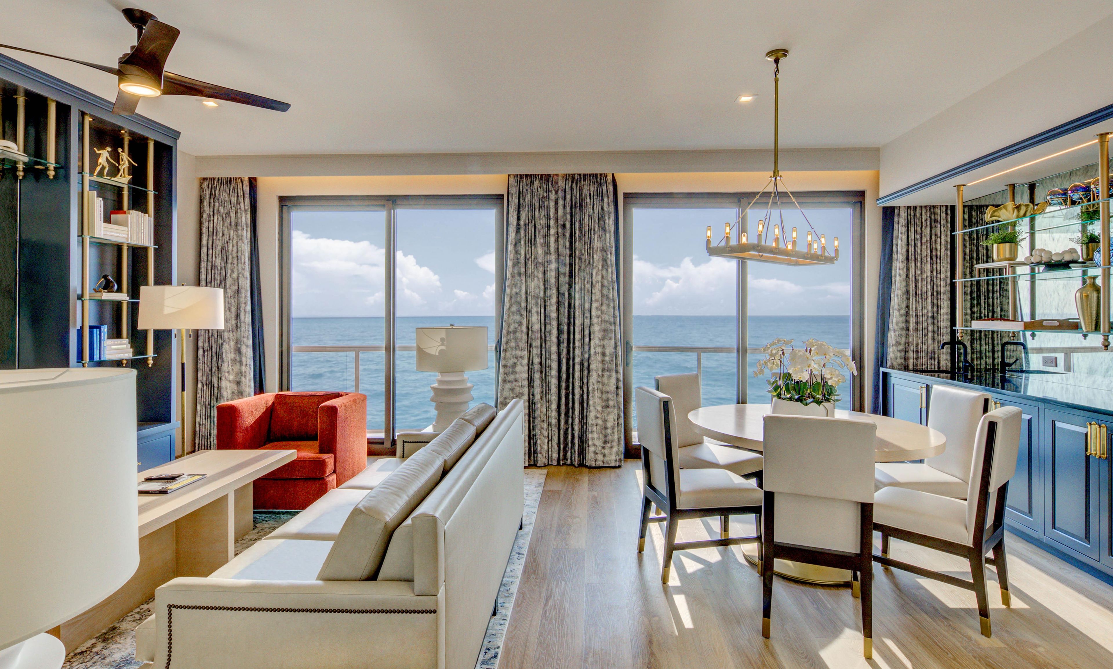 A modern living room with a view of the sea, a dining area, and a kitchen with a glass display case.