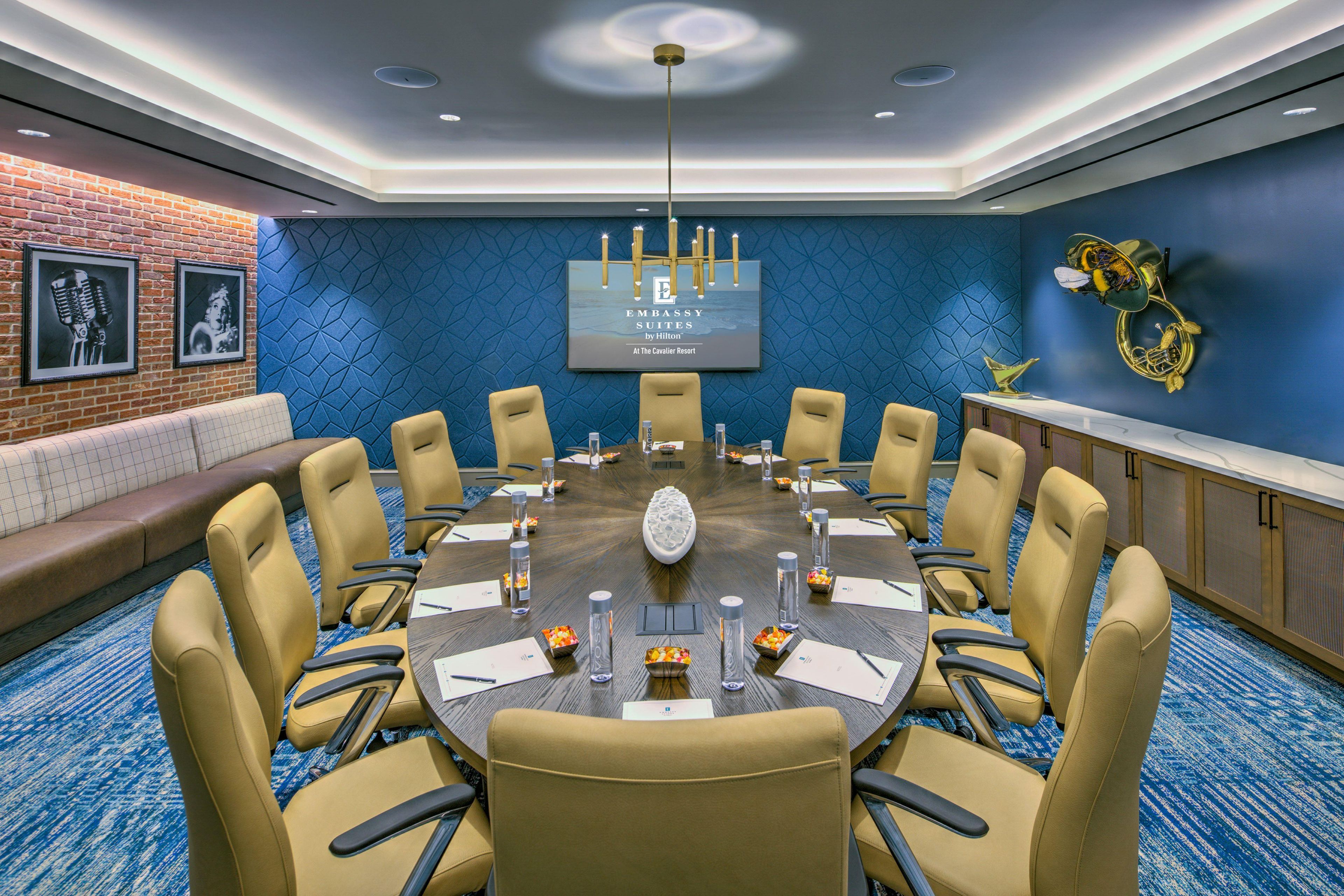A conference room with a long table, chairs, a screen, and a blue textured wall.