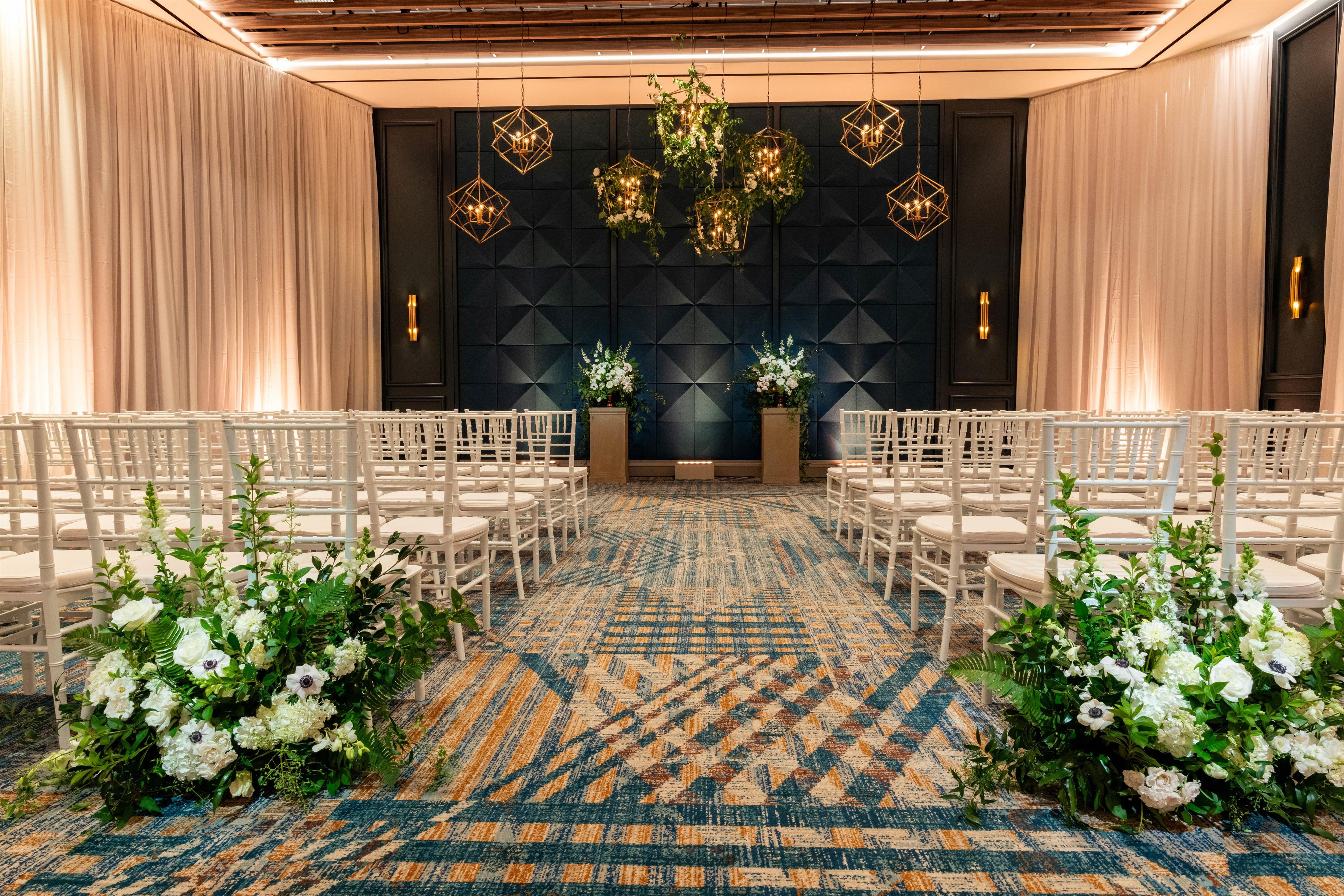 Een elegante evenementenruimte met witte stoelen in rijen, een kamerbreed tapijt en decoratieve verlichtingsarmaturen.