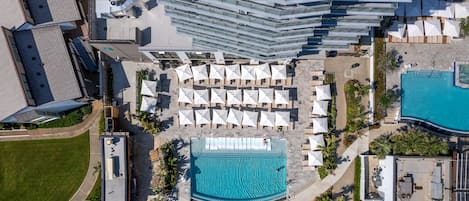 Oversigtsbillede af et hotel med swimmingpool, flere loungeområder med parasoller, og moderne arkitektur.