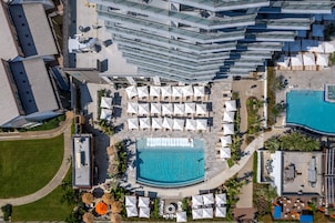 Vista aérea de um hotel com piscina, várias áreas de descanso com guarda-sóis e design arquitetônico moderno.