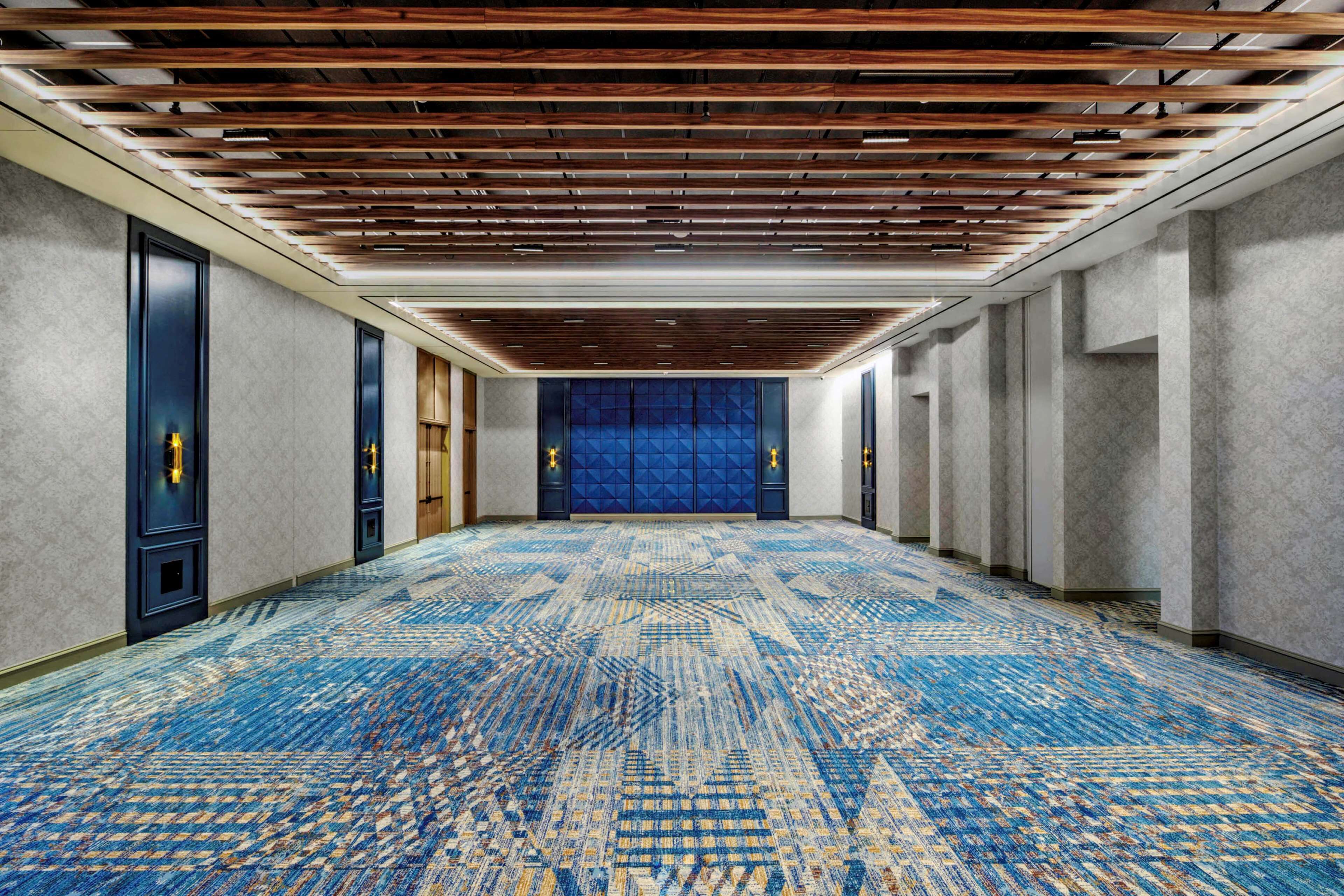 A hallway with a patterned carpet, wooden ceiling beams, and doors with golden accents.