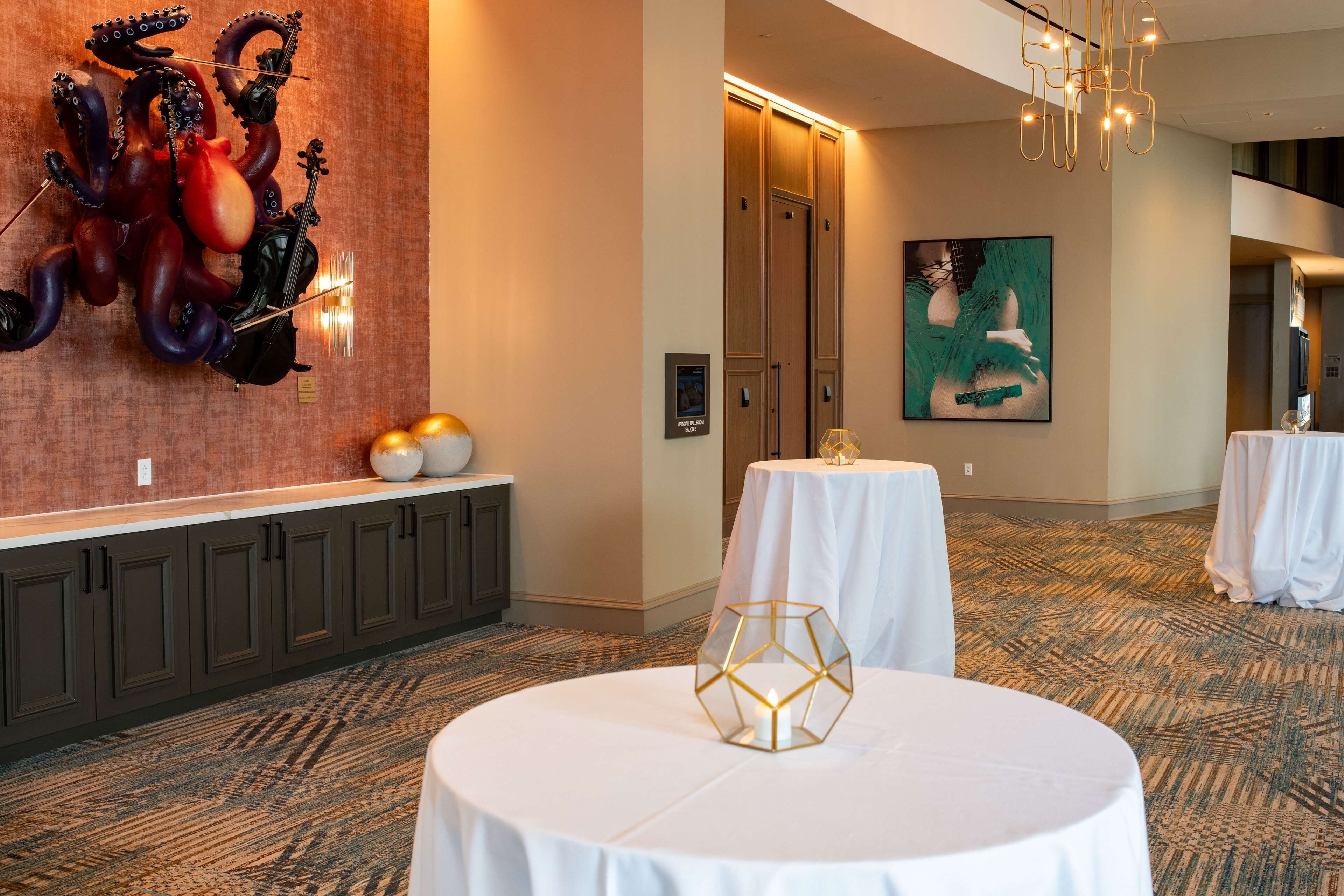 A hotel lobby with a round table, a decorative wall piece, and a large painting.