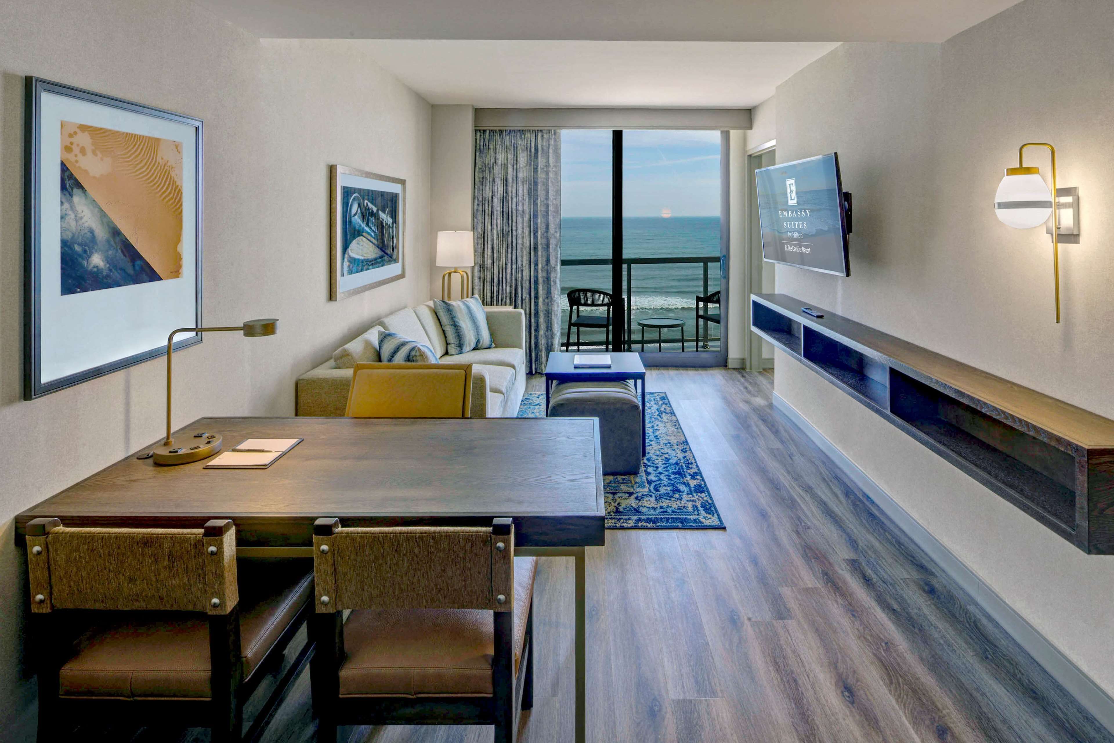 Ein modernes Hotelzimmer mit Essbereich, einer Couch, einem Fernseher und Blick aufs Meer.