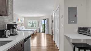 A modern kitchen with a dishwasher, toaster, and coffee maker. A dining area with a bench and curtains is visible in the background. - 1407 - Universal Studios View (Orlando)