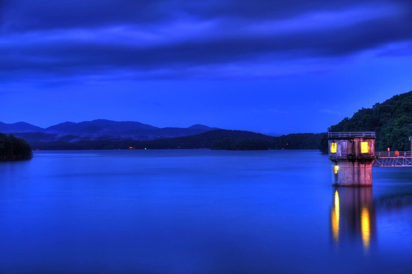 A calm lake at dusk with a dock and a small building on the right.