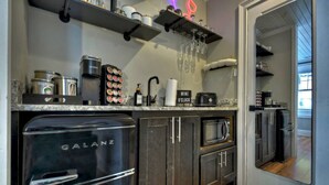 A compact kitchen with a Galanz oven, a coffee machine, and a microwave. There are shelves with jars and a wine o'clock sign. - Modern Penthouse Suite in historic downtown Blue Ridge, GA (Blue Ridge)