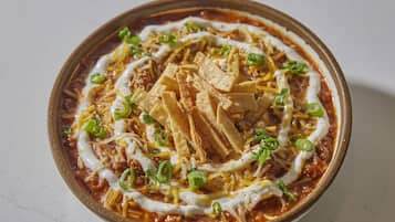 A bowl of nachos topped with cheese, sour cream, and green onions.