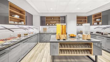 A modern kitchen with built-in shelves, a central island with glassware, and a variety of food items on the counter.