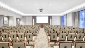 A conference room with rows of chairs facing a large screen, a podium, and a carpeted floor.