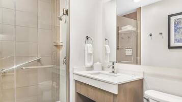 A modern bathroom with a glass shower enclosure, a white sink, and a wooden vanity.
