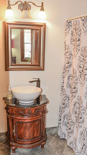 A bathroom with a wooden vanity, a white sink, and a mirror above it. There is a shower curtain with a floral pattern.