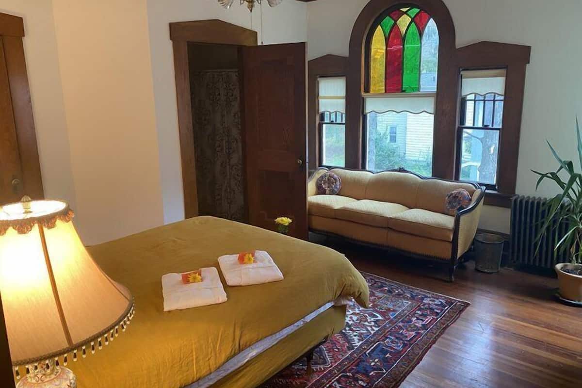 A room with a bed, a sofa, a chandelier, a stained glass window, and a radiator.