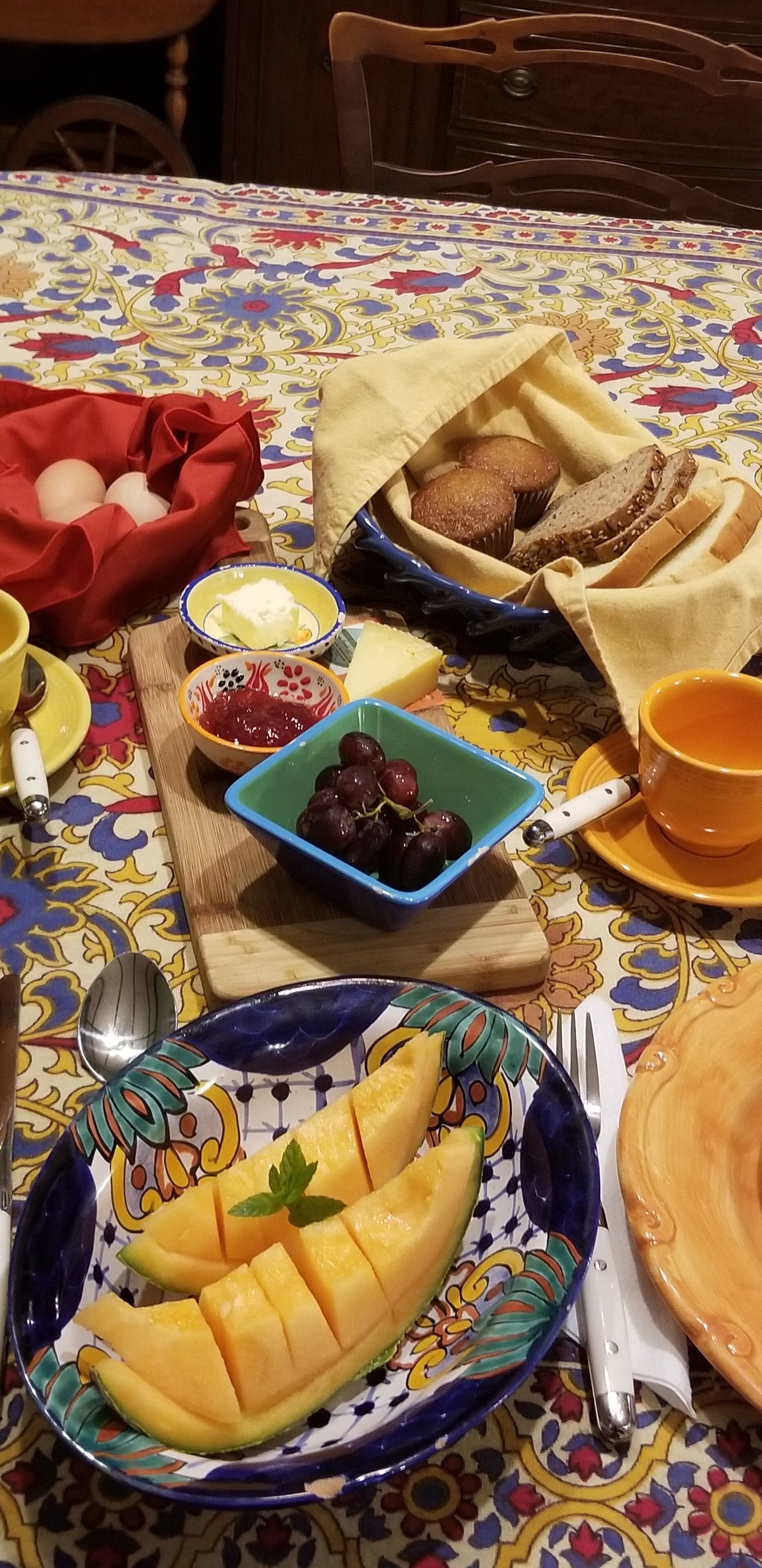 A table set with a variety of food items including bread, muffins, eggs, and fruit.