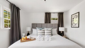 A neatly made bed with a grey headboard, two bedside lamps, a tray with breakfast items, and a framed abstract artwork on the wall. - Beautiful Backyard! | Angel Oak in Park Circle (North Charleston)