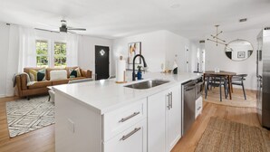 A modern kitchen with white cabinetry, a central island, and a dining area with a round table and chairs. - Beautiful Backyard! | Angel Oak in Park Circle (North Charleston)