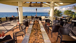 Relax on the ocean-view patio, surrounded by wicker chairs and tables, under a shaded pergola.