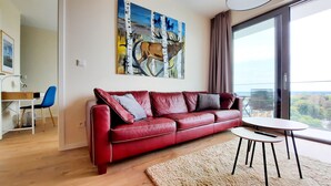 Ein rotes Ledersofa mit Kissen, ein kleiner runder Tisch und ein Bild eines Elchs an der Wand.