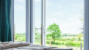 Een kamer met een groot raam, uitzicht op een groen landschap en een houten plafond.