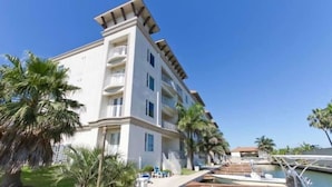 Ein mehrstöckiges Hotel mit Balkonen, eine Marina mit Booten und Palmen.