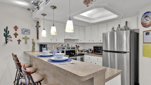 Eine moderne Küche mit weißen Schränken, einem Edelstahlkühlschrank, Pendelleuchten und einer zentralen Kochinsel mit Barhocker.