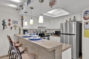 Una cocina moderna con armarios blancos, un refrigerador de acero inoxidable, luces colgantes y una isla central con taburetes de bar.