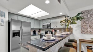 A modern kitchen with a central island, stainless steel appliances, and a decorative plant. - Beach Steps Away: Garden Oasis with Pool & Jacuzzi (South Padre Island)